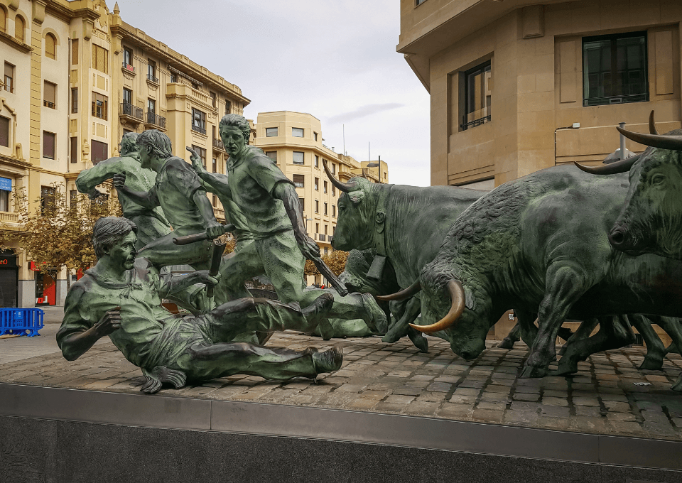 Escultura en bronce que homenajea los encierros de San Fermín en Pamplona, con figuras de corredores y toros en plena carrera